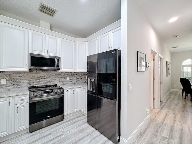 kitchen with light wood-type flooring, tasteful backsplash, light stone counters, white cabinetry, and stainless steel appliances