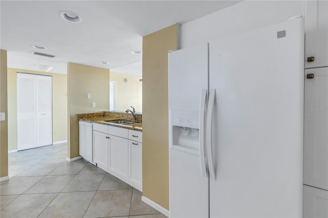 kitchen featuring white appliances, sink, dark stone countertops, light tile patterned flooring, and white cabinetry