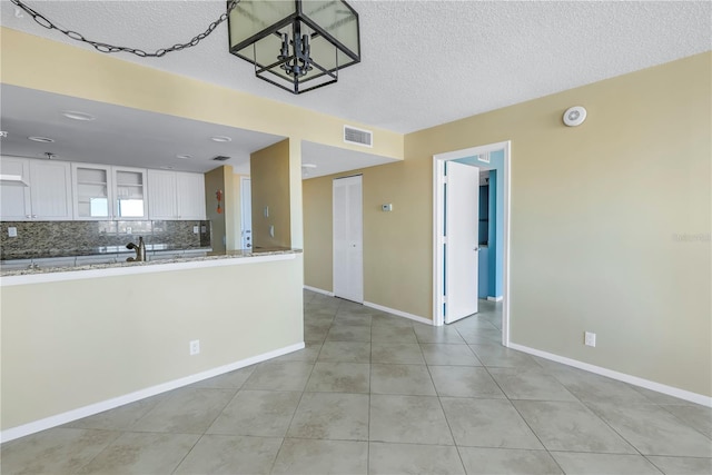 kitchen with light stone countertops, backsplash, white cabinets, a chandelier, and light tile patterned flooring