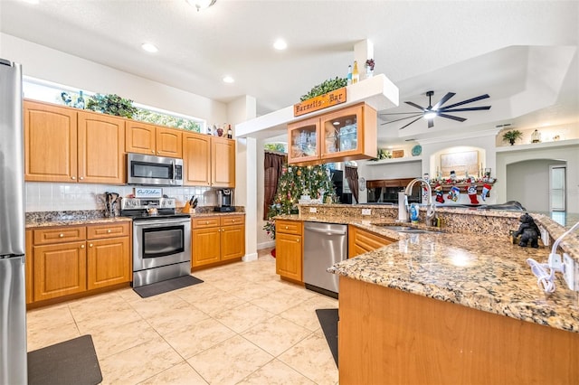 kitchen with sink, ceiling fan, light stone countertops, kitchen peninsula, and stainless steel appliances