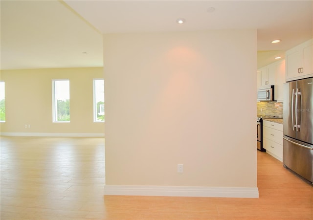 kitchen with tasteful backsplash, white cabinets, appliances with stainless steel finishes, and light hardwood / wood-style flooring