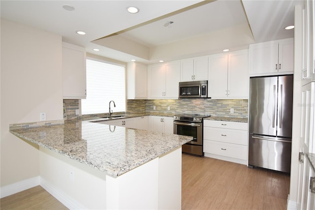 kitchen with kitchen peninsula, sink, stainless steel appliances, and white cabinetry