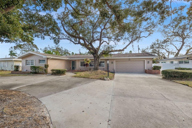 ranch-style house featuring a garage, driveway, fence, and stucco siding