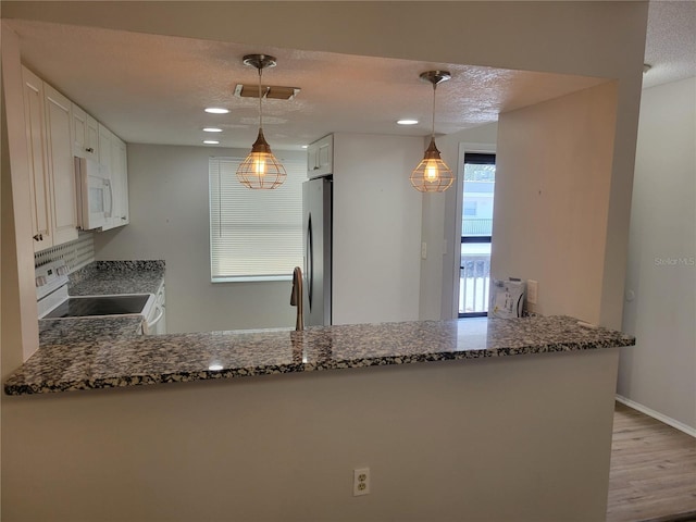 kitchen featuring kitchen peninsula, stainless steel fridge, pendant lighting, white cabinets, and range