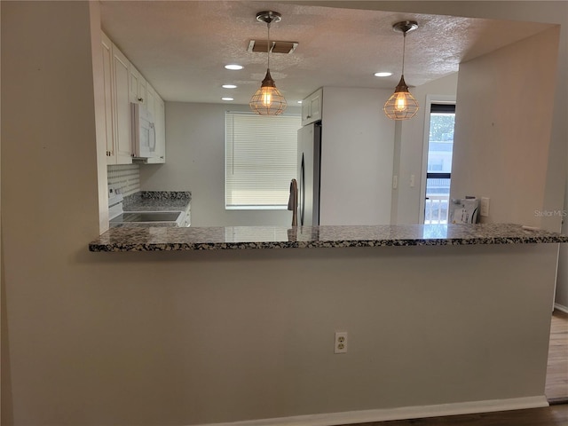 kitchen with kitchen peninsula, appliances with stainless steel finishes, white cabinets, and pendant lighting