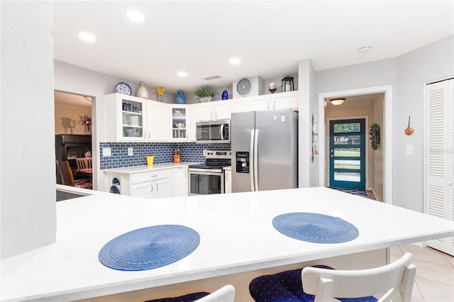 kitchen featuring appliances with stainless steel finishes, white cabinets, a kitchen breakfast bar, decorative backsplash, and kitchen peninsula