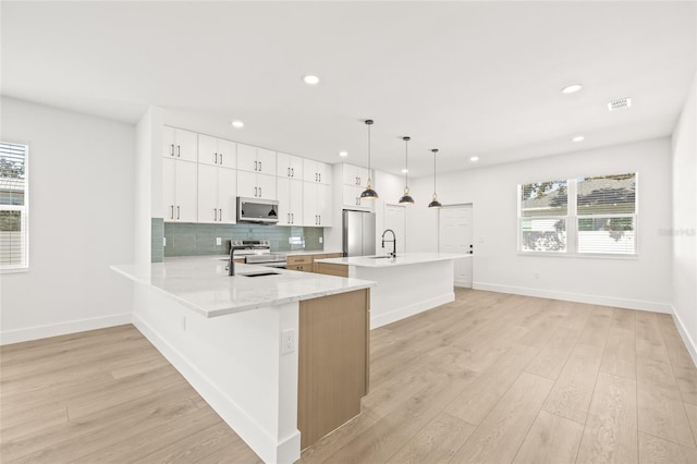 kitchen with white cabinetry, light hardwood / wood-style flooring, kitchen peninsula, decorative light fixtures, and appliances with stainless steel finishes