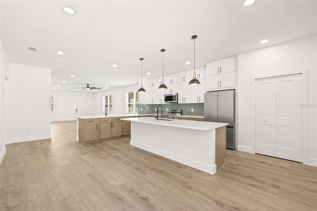 kitchen with stainless steel appliances, ceiling fan, a large island with sink, light hardwood / wood-style flooring, and white cabinetry