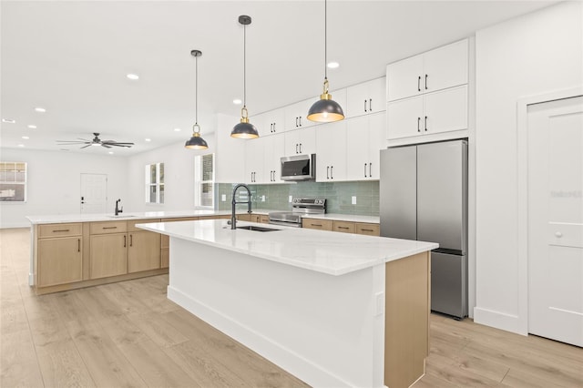 kitchen with ceiling fan, sink, stainless steel appliances, a kitchen island with sink, and light wood-type flooring