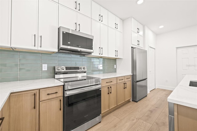 kitchen with backsplash, white cabinets, light wood-type flooring, appliances with stainless steel finishes, and light stone counters