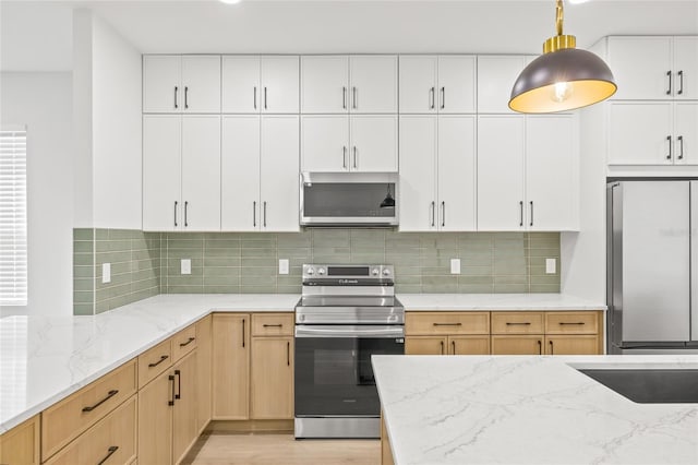 kitchen with tasteful backsplash, white cabinets, pendant lighting, and appliances with stainless steel finishes