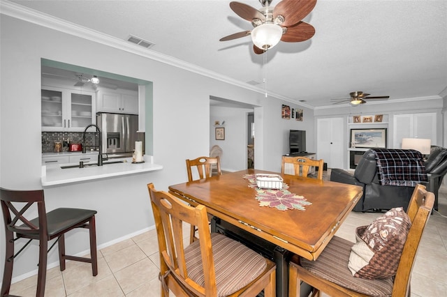 tiled dining space featuring crown molding, ceiling fan, sink, and a textured ceiling