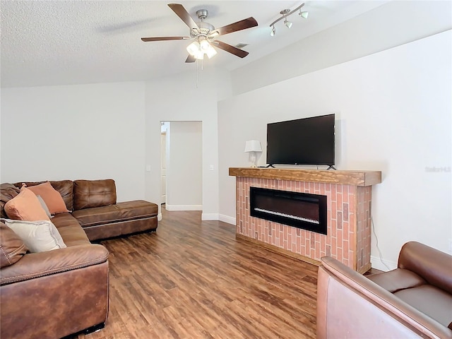 living room with ceiling fan, wood-type flooring, a textured ceiling, and a brick fireplace