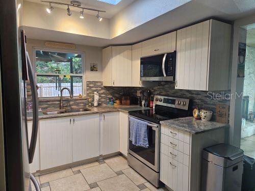 kitchen with appliances with stainless steel finishes, a skylight, tasteful backsplash, and white cabinetry