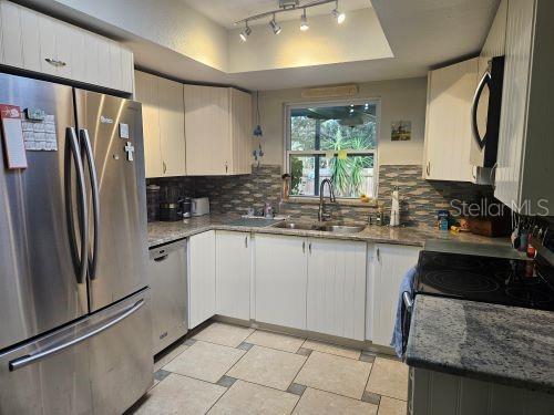 kitchen with stainless steel appliances, stone countertops, white cabinets, and sink