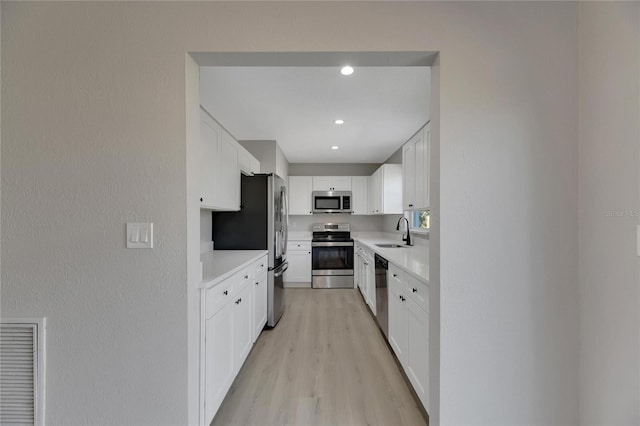 kitchen featuring appliances with stainless steel finishes, light hardwood / wood-style flooring, white cabinetry, and sink