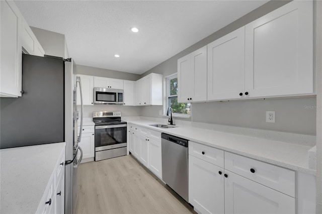 kitchen featuring white cabinets, appliances with stainless steel finishes, light wood-type flooring, and sink