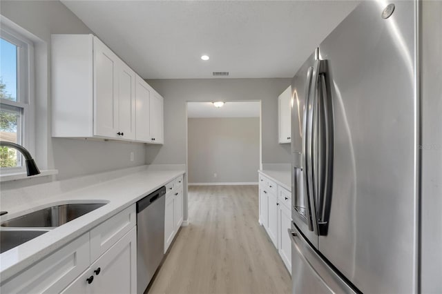 kitchen with appliances with stainless steel finishes, light wood-type flooring, white cabinetry, and sink