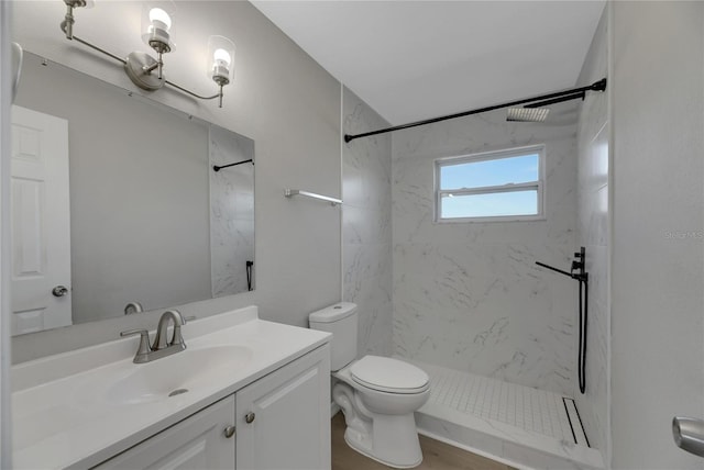 bathroom featuring vanity, toilet, a tile shower, and wood-type flooring