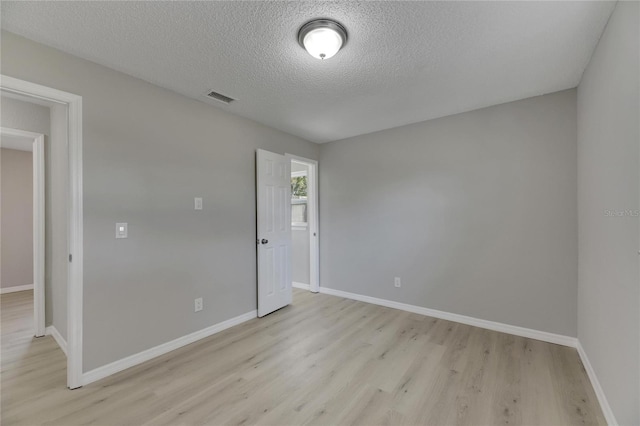 empty room with a textured ceiling and light hardwood / wood-style floors