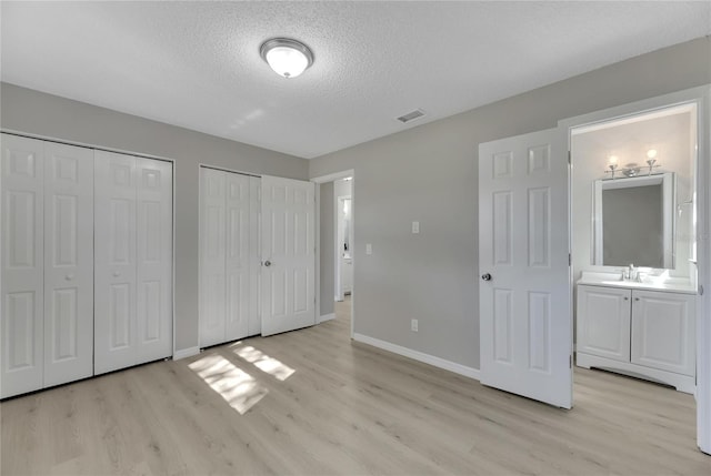 unfurnished bedroom with two closets, sink, light hardwood / wood-style flooring, ensuite bath, and a textured ceiling