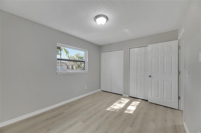 unfurnished bedroom with multiple closets, light hardwood / wood-style flooring, and a textured ceiling