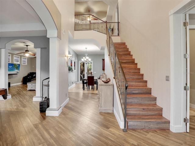 foyer entrance featuring ceiling fan with notable chandelier, light hardwood / wood-style floors, and a towering ceiling