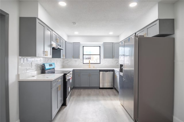 kitchen featuring a textured ceiling, stainless steel appliances, sink, backsplash, and gray cabinets