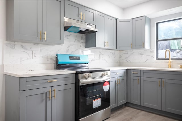 kitchen with tasteful backsplash, light hardwood / wood-style floors, sink, electric range, and gray cabinetry