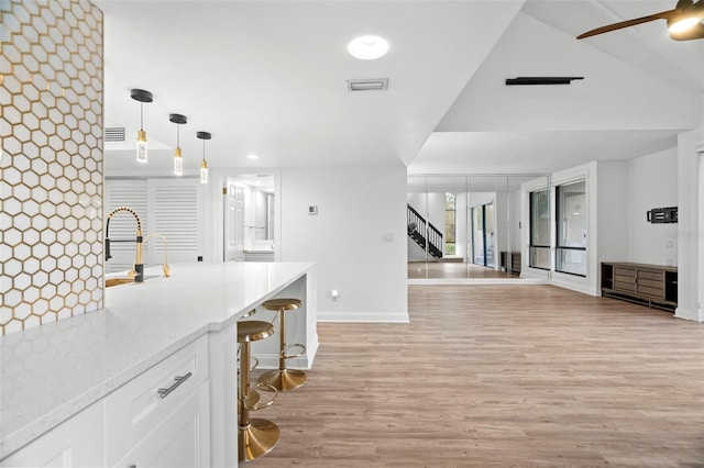 kitchen with pendant lighting, white cabinets, a kitchen breakfast bar, light hardwood / wood-style flooring, and light stone counters