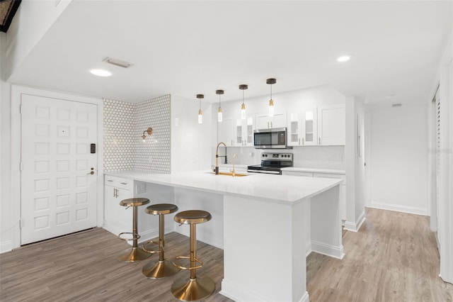 kitchen with a kitchen bar, appliances with stainless steel finishes, light wood-type flooring, pendant lighting, and white cabinetry