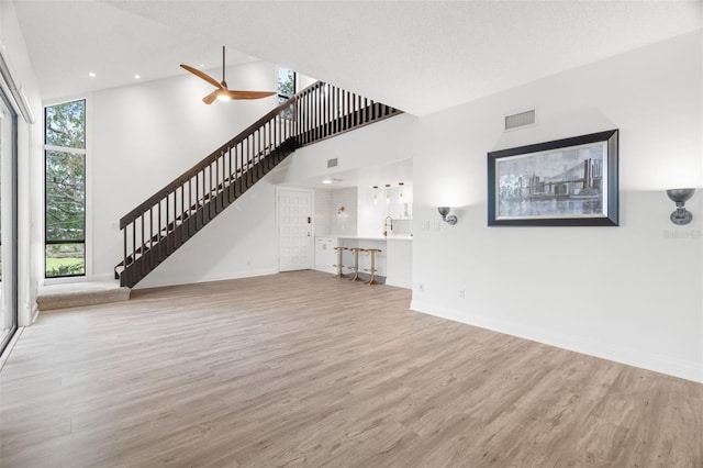 unfurnished living room featuring ceiling fan, a towering ceiling, a textured ceiling, and light wood-type flooring