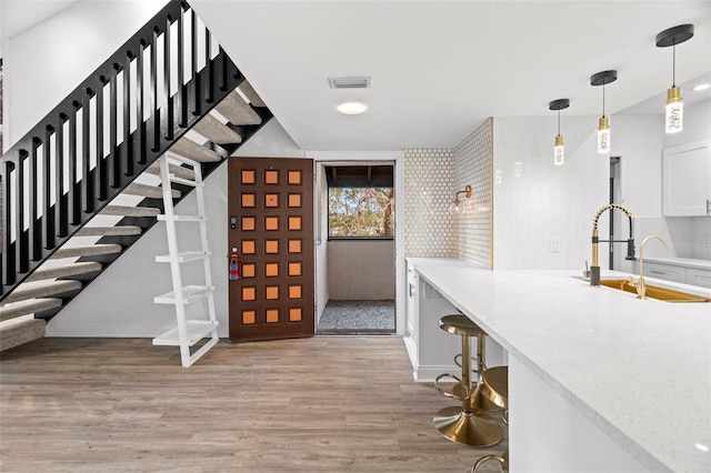 interior space with backsplash, sink, decorative light fixtures, light hardwood / wood-style floors, and white cabinetry