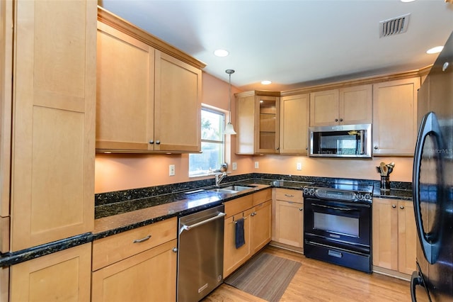 kitchen with pendant lighting, dark stone counters, black appliances, sink, and light wood-type flooring