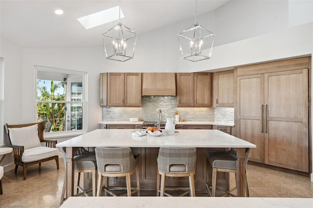 kitchen featuring a center island with sink, vaulted ceiling with skylight, and wall chimney exhaust hood