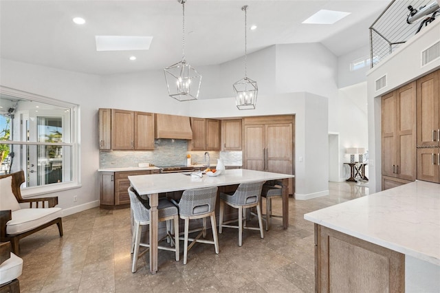 kitchen featuring premium range hood, decorative light fixtures, a skylight, and high vaulted ceiling