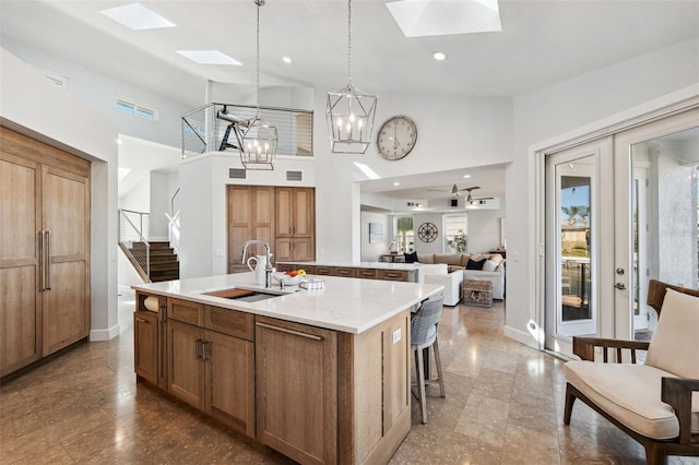 kitchen featuring pendant lighting, sink, a kitchen island with sink, a skylight, and a high ceiling