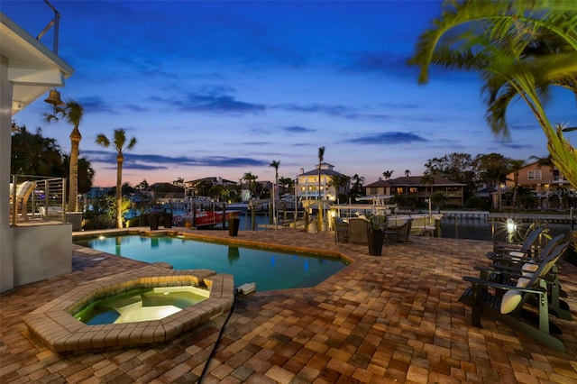 pool at dusk featuring a water view, an in ground hot tub, and a patio