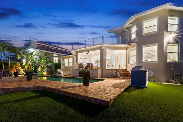 back house at dusk with a balcony, a lawn, ceiling fan, and a patio area