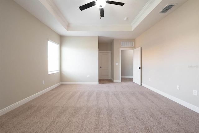 spare room with a raised ceiling, light carpet, ceiling fan, and ornamental molding