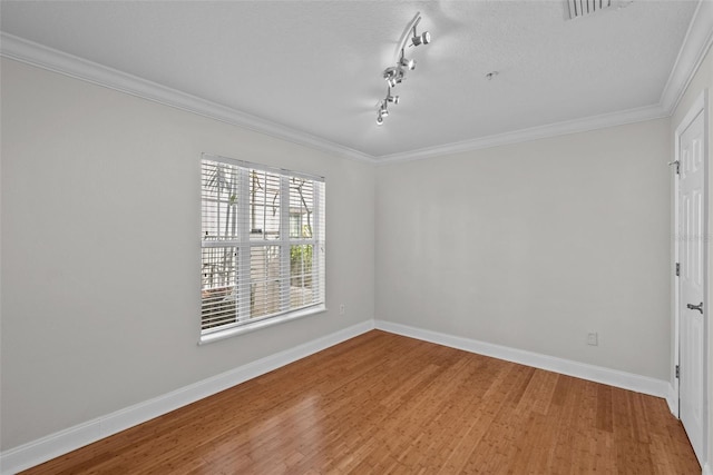 empty room featuring hardwood / wood-style flooring, track lighting, ornamental molding, and a textured ceiling