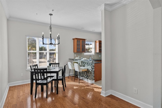 dining area featuring hardwood / wood-style flooring, crown molding, sink, and a notable chandelier