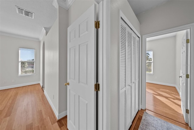 hallway with ornamental molding, light hardwood / wood-style floors, and a textured ceiling