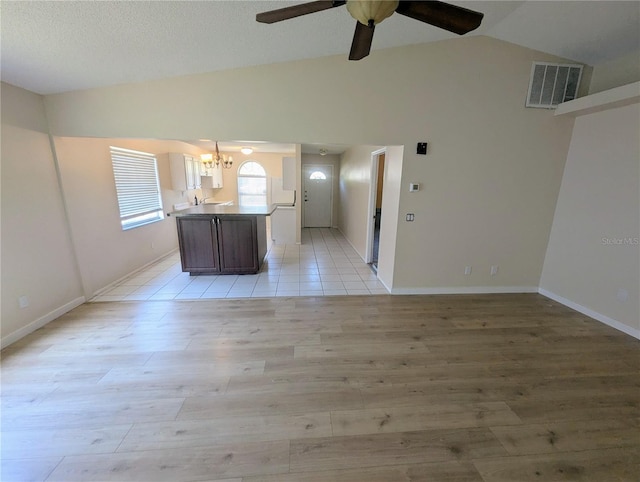 unfurnished living room with light hardwood / wood-style flooring, ceiling fan with notable chandelier, and vaulted ceiling