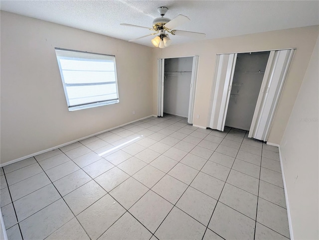 unfurnished bedroom with ceiling fan, light tile patterned flooring, a textured ceiling, and multiple closets