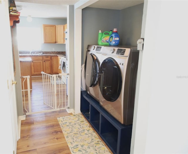 clothes washing area with washer and dryer, light wood-type flooring, and sink