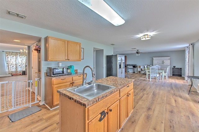 kitchen featuring sink, stainless steel fridge, ceiling fan, a center island with sink, and light hardwood / wood-style flooring