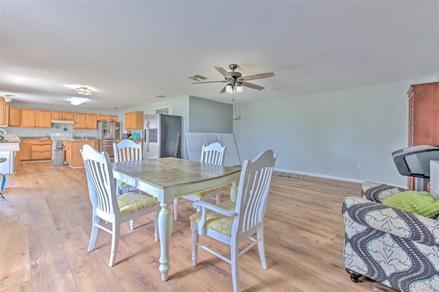 dining room with sink, light hardwood / wood-style floors, a textured ceiling, and ceiling fan