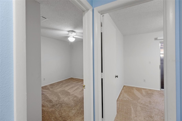 corridor with a textured ceiling and light carpet