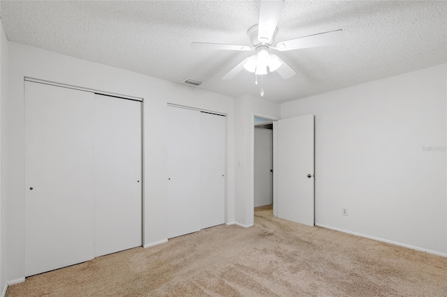 unfurnished bedroom with a textured ceiling, ceiling fan, light carpet, and two closets